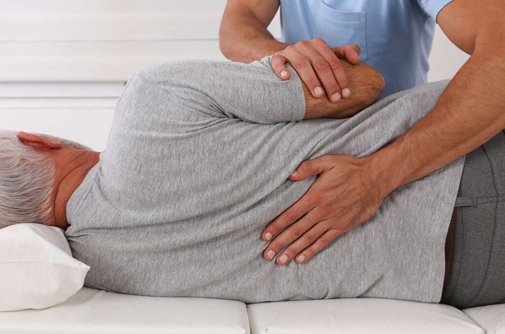 A therapist guides an adult through a controlled stretching and strengthening exercise in a bright clinic room.